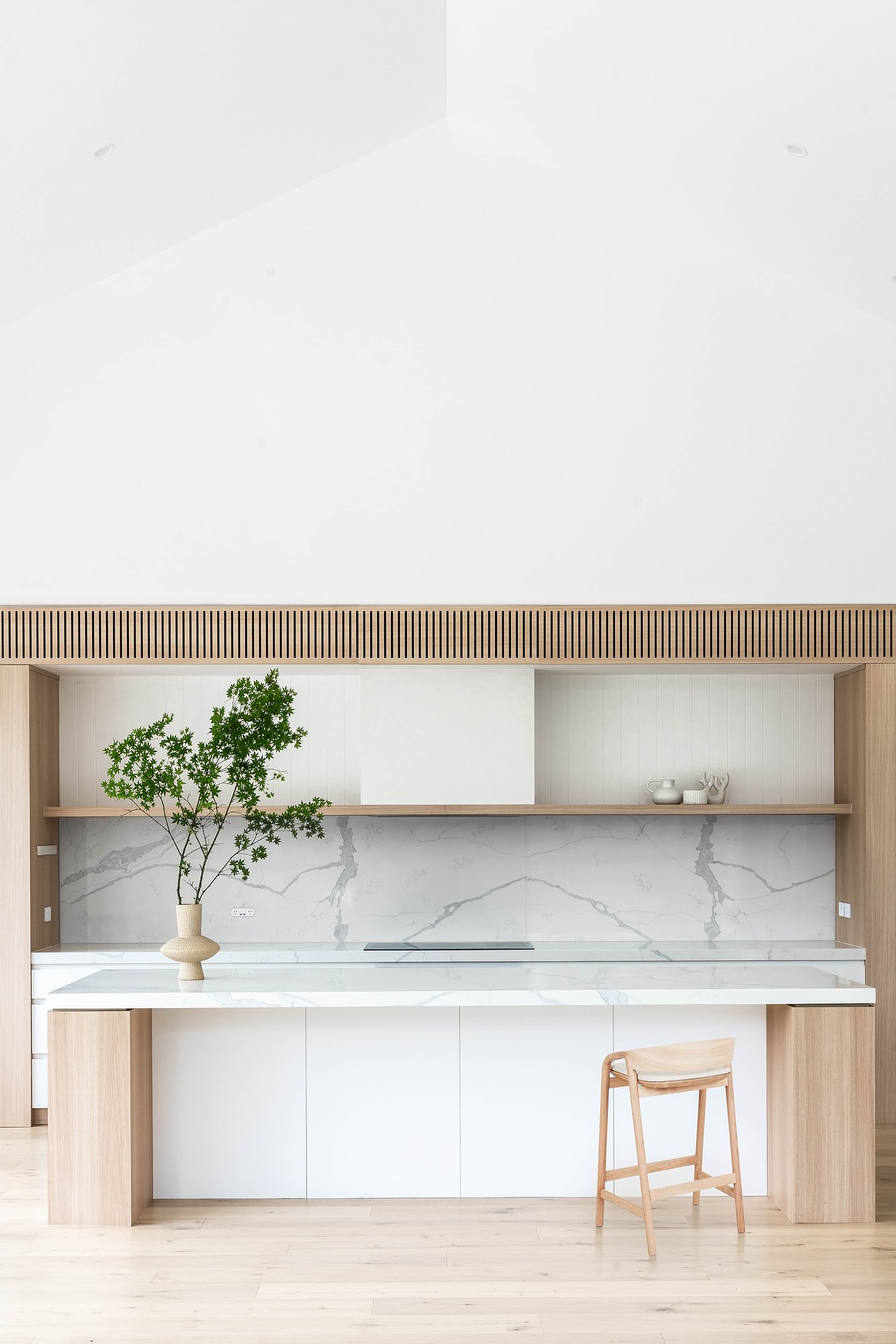 Kitchen with fluted timber overhead joinery, Carrara marble island benchtop, and white cabinetry beneath timber shelving.