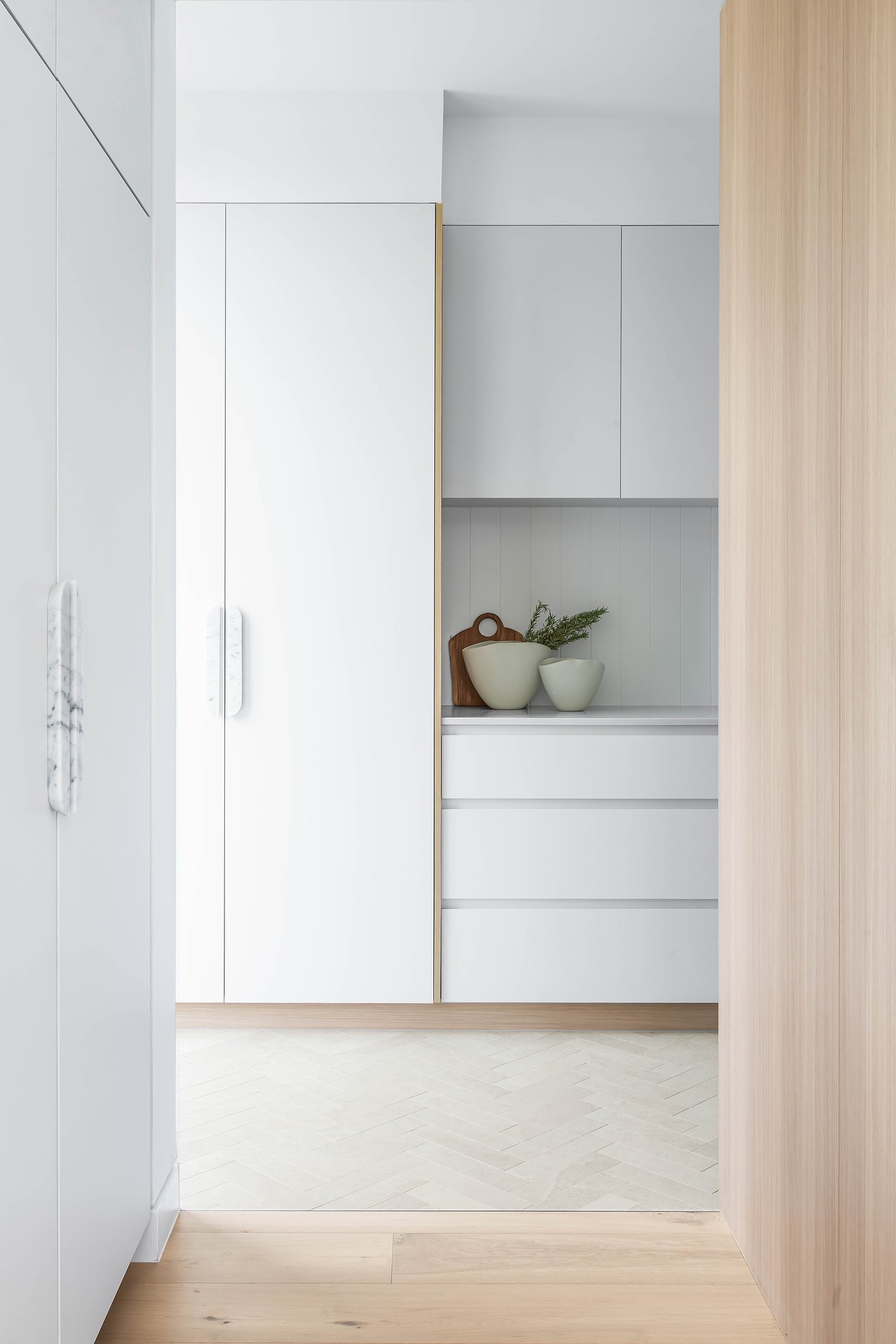 White kitchen cabinetry with integrated timber detailing and open shelving displaying ceramics.