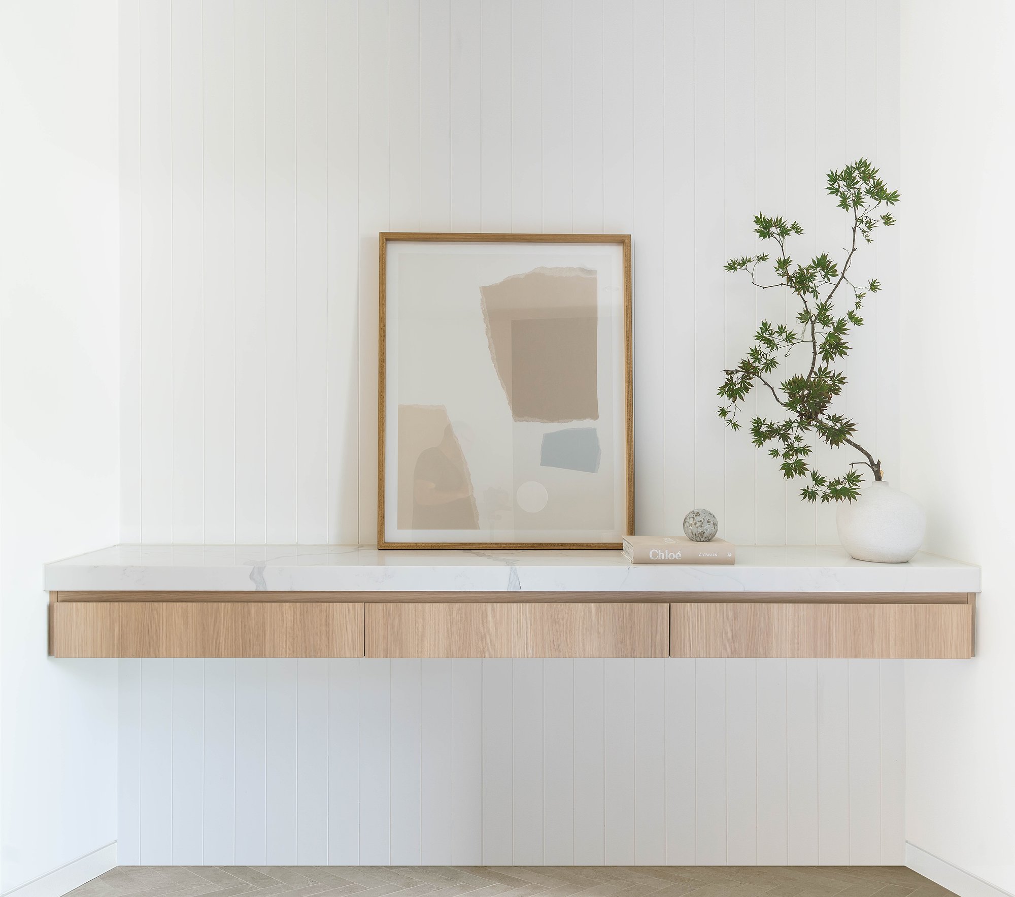 Floating American oak console with white vase and framed artwork against white wall.