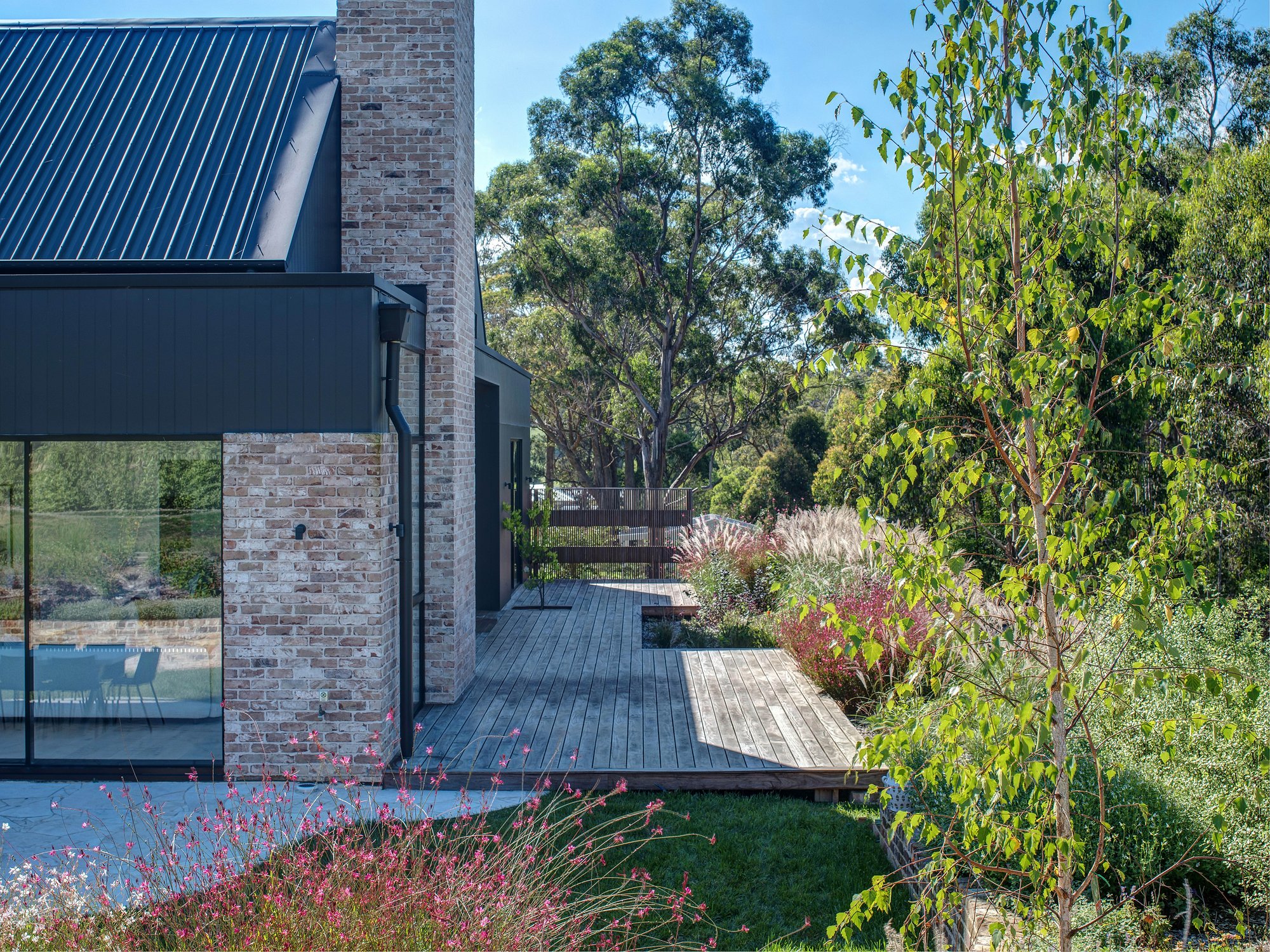 Modern pavilion home with recycled brick and dark metal cladding opens to perennial gardens via expansive glazing and timber deck.