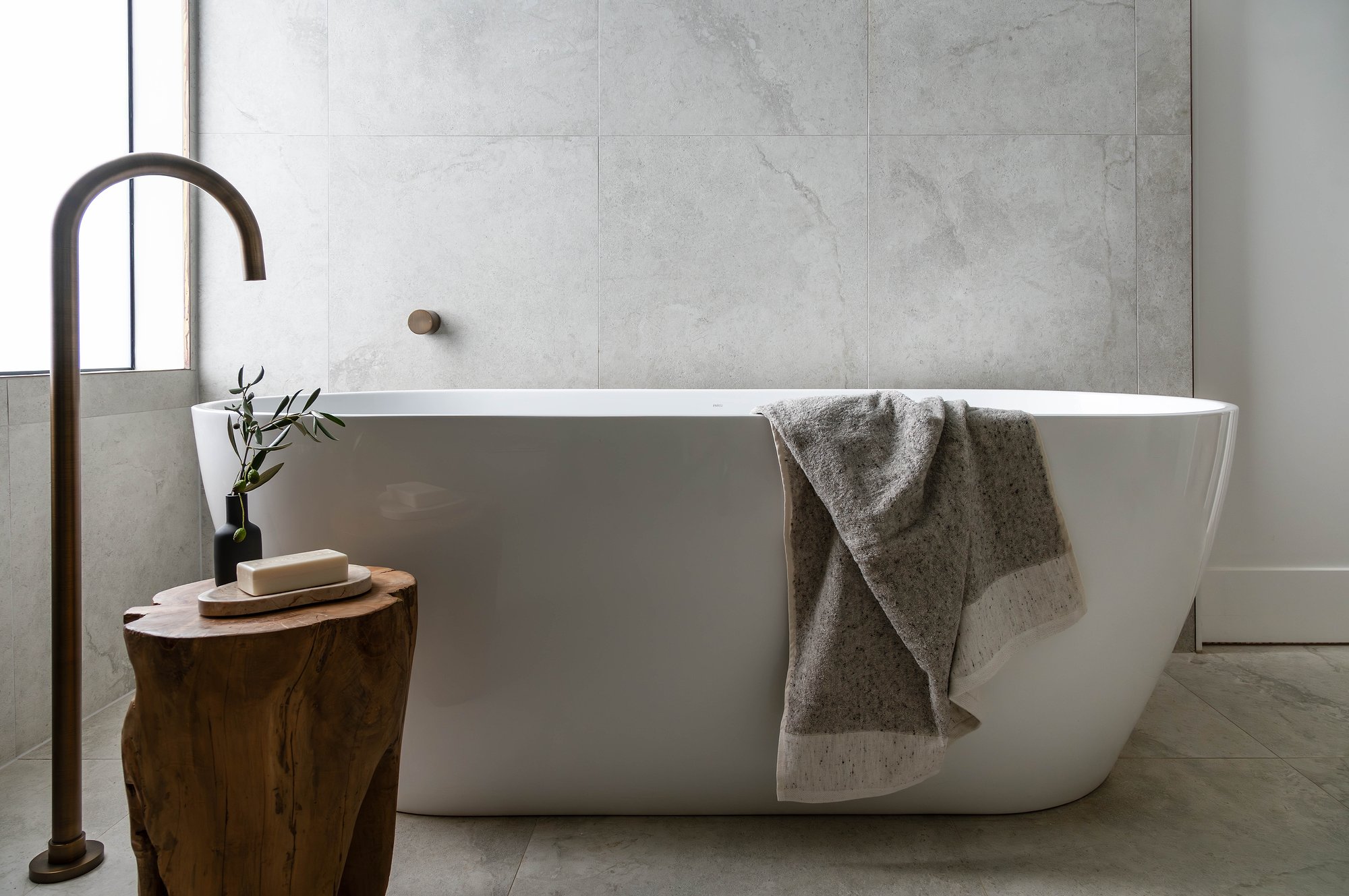 Freestanding bath in Carrara marble bathroom with brass floor-mounted tapware and natural stone wall tiling.