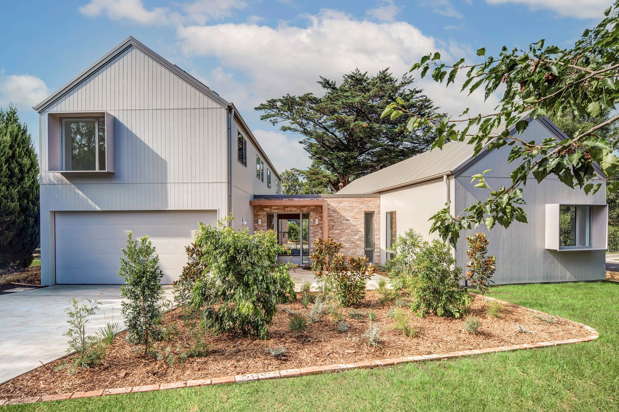 White weatherboard pavilion with recycled brick and steel-framed glazing set within established Southern Highlands gardens.