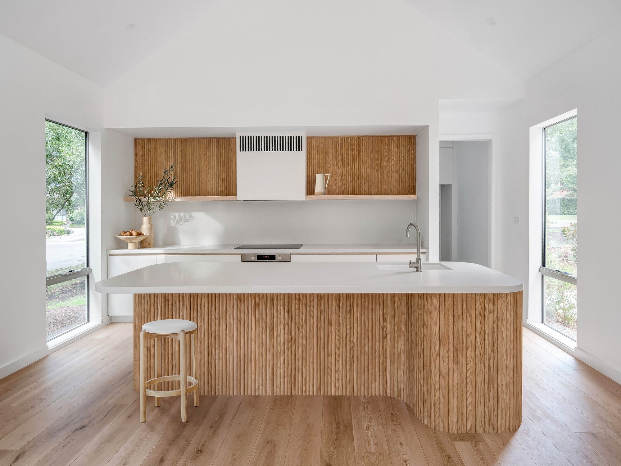 Open kitchen with American oak joinery and island, Carrara marble benchtop, timber floors extending to garden views through floor-to-ceiling glazing.