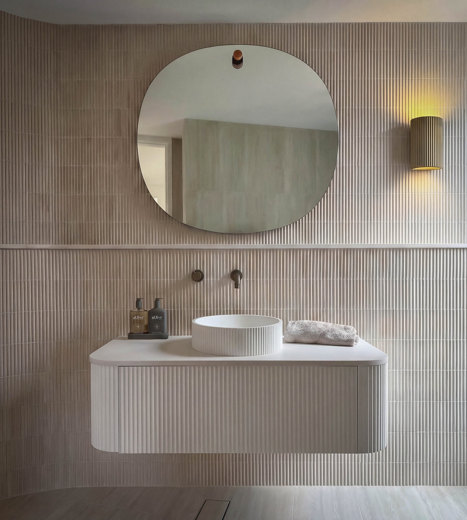 Floating vanity in fluted timber with vessel basin, brass tapware, and circular mirror against vertical timber panelling.