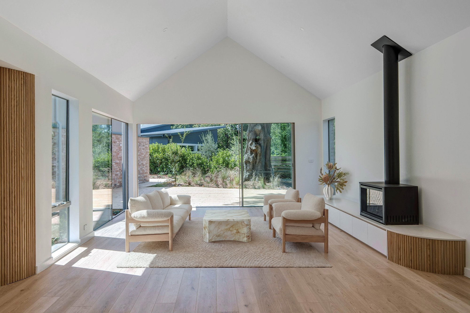Open-plan living room with American oak flooring, black steel fireplace, and expansive glazing to landscaped courtyard.