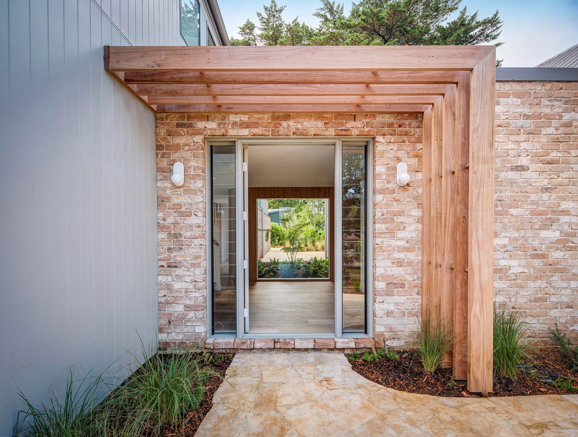 Recycled brick entry with timber pergola and glazed front door revealing interior courtyard beyond.