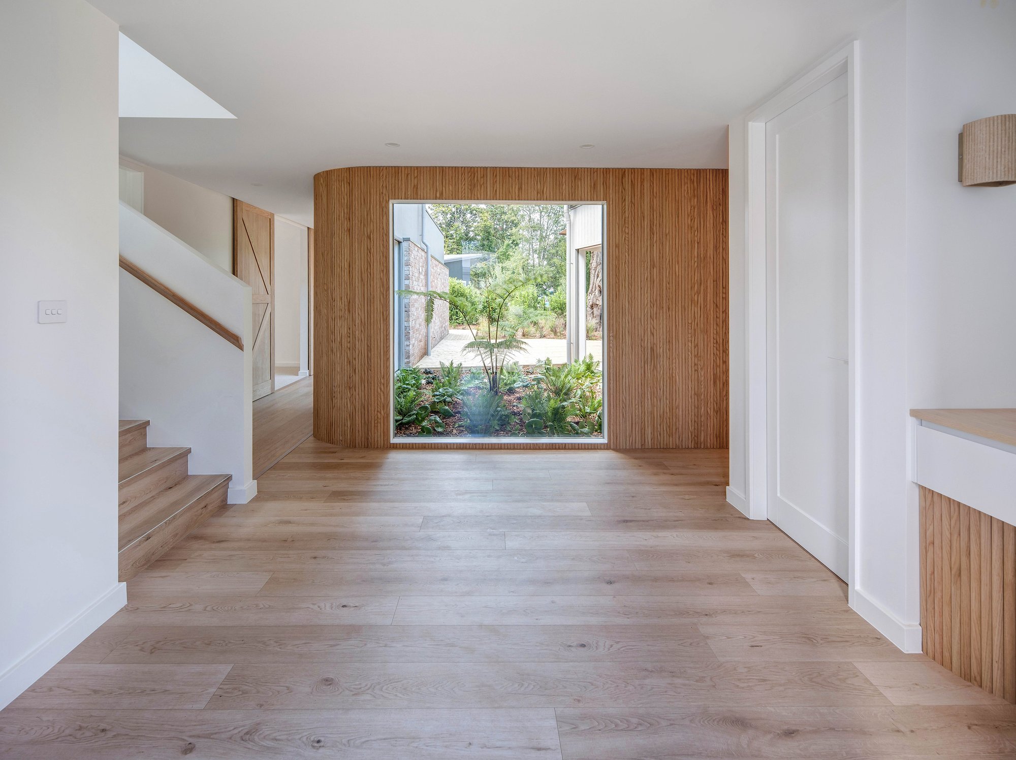 Open-plan living space with American oak feature wall framing garden window, pale timber floors throughout.