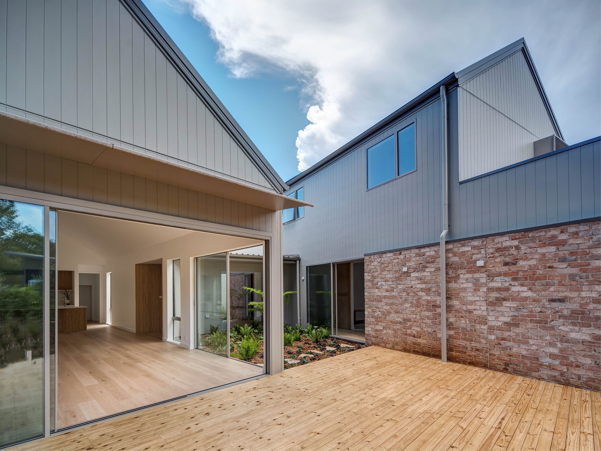 Timber deck extends from glazed pavilion, connecting to contemporary home with recycled brick and metal cladding.