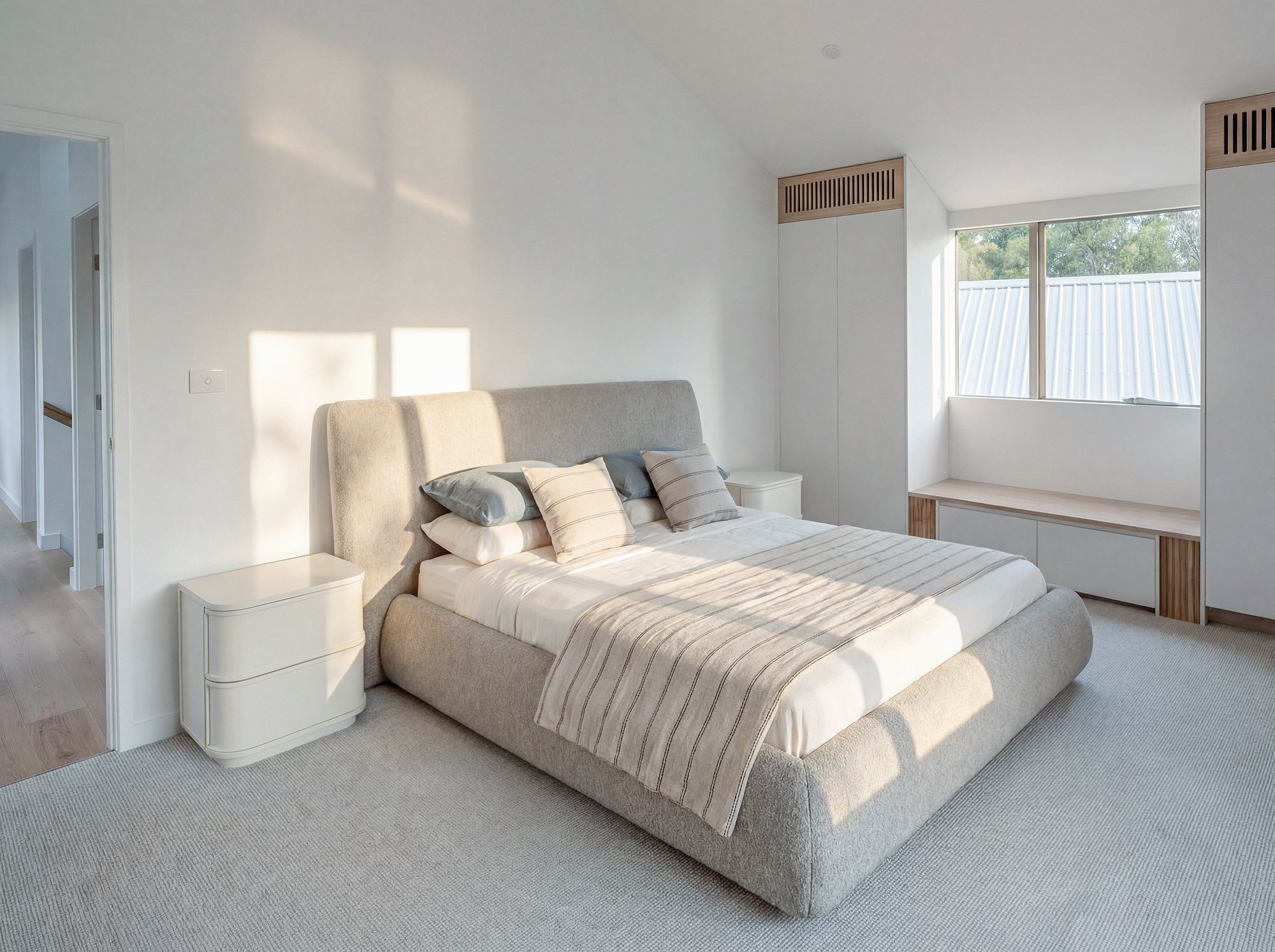 Minimalist bedroom with upholstered platform bed, built-in timber joinery, and garden outlook through full-height glazing.