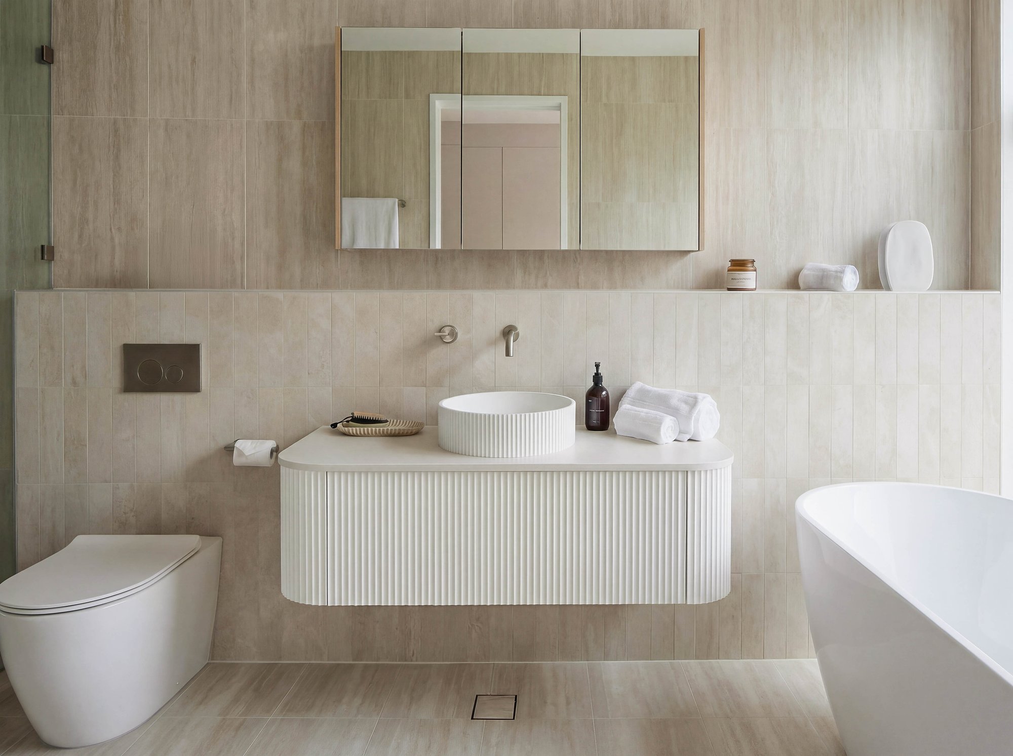 Contemporary bathroom with fluted timber vanity, integrated basin, and neutral stone finishes throughout.