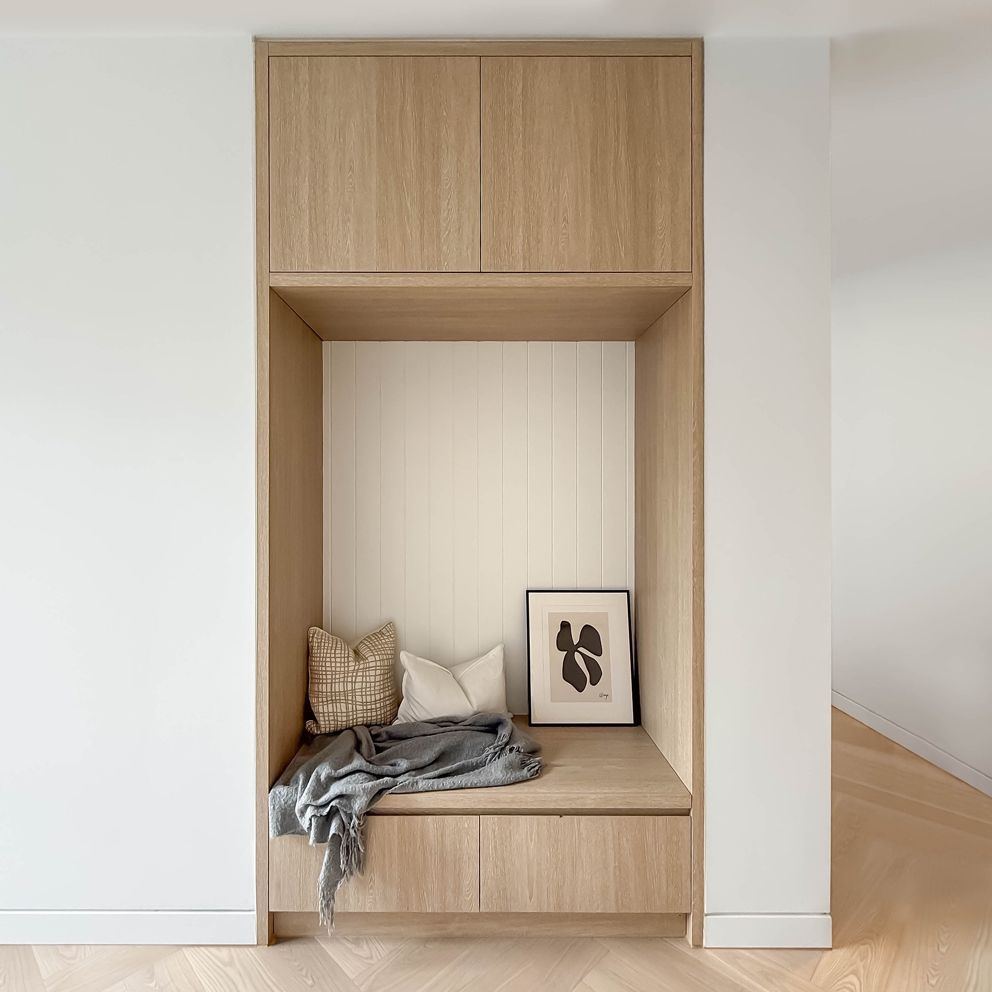 Built-in timber reading nook with overhead storage, featuring natural oak joinery and integrated bench seating.