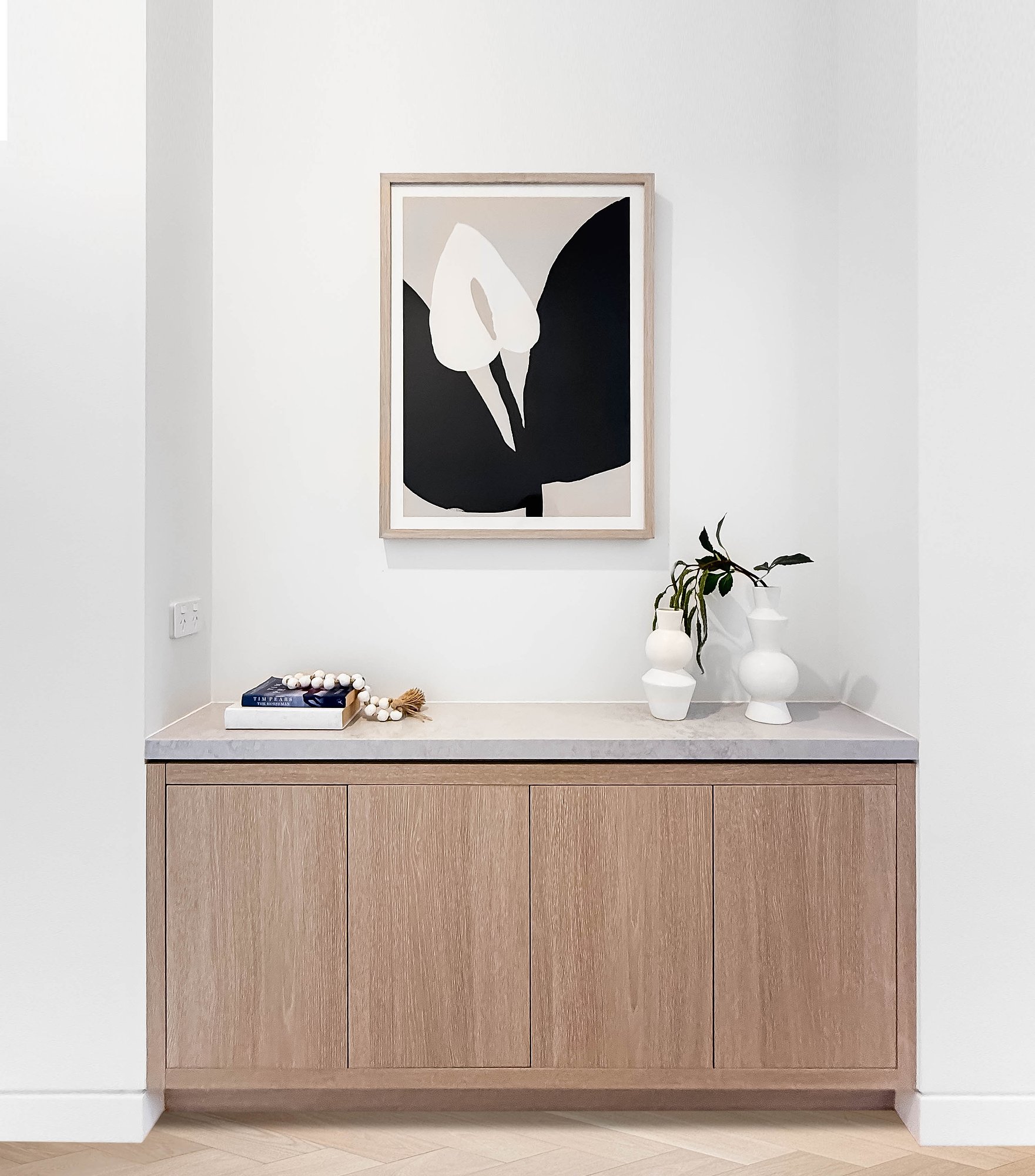 Floating console in American oak with concrete benchtop, displaying abstract botanical artwork and ceramic vessels.