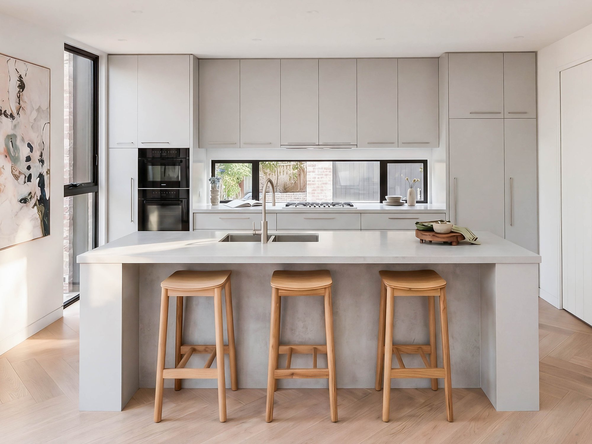 Kitchen with concrete benchtop island, timber bar stools, and integrated joinery in neutral tones.