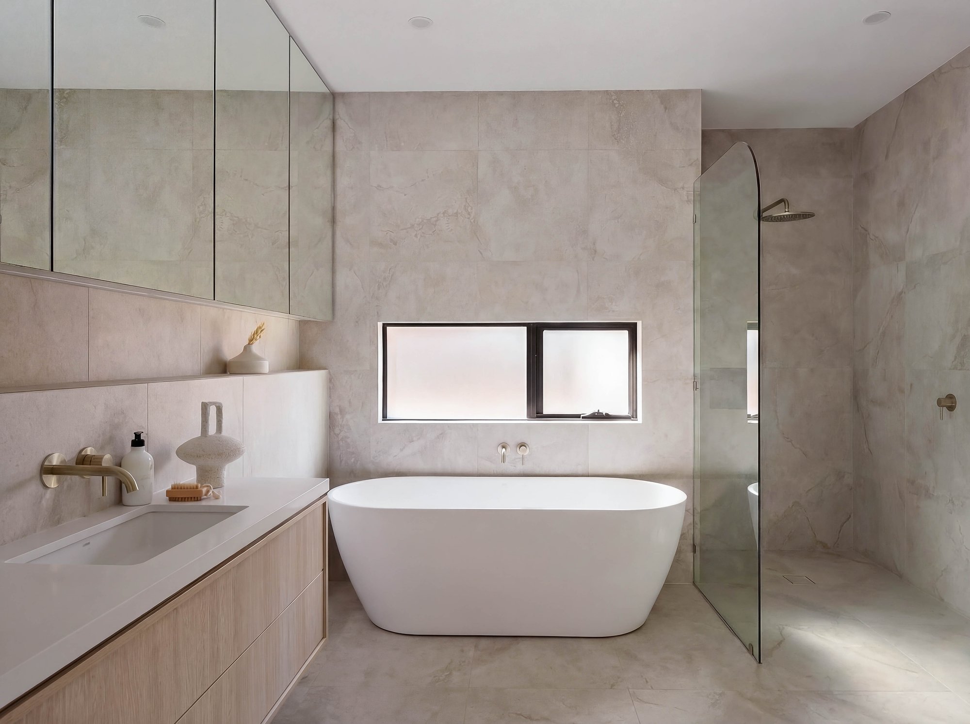 Contemporary bathroom with freestanding white bathtub, travertine walls, and timber vanity with integrated basin.