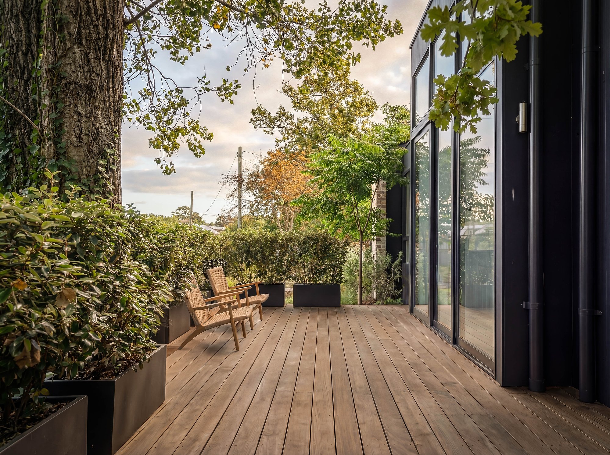 Timber deck terrace with glazed pavilion facade, established plantings frame views across the Southern Highlands landscape.