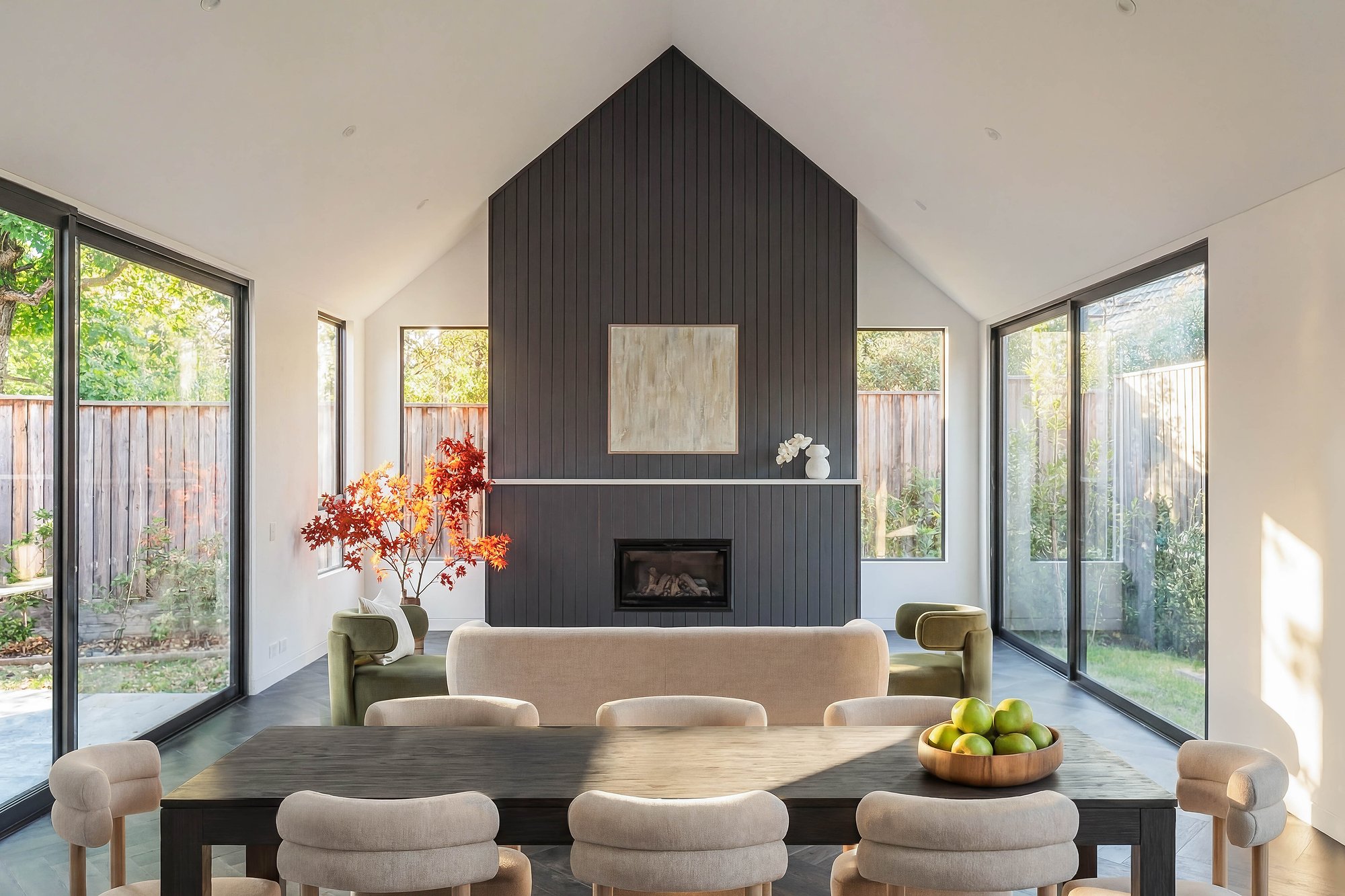 Open-plan living with charcoal-painted chimney breast, recycled brick hearth, and floor-to-ceiling glazing framing established garden views.