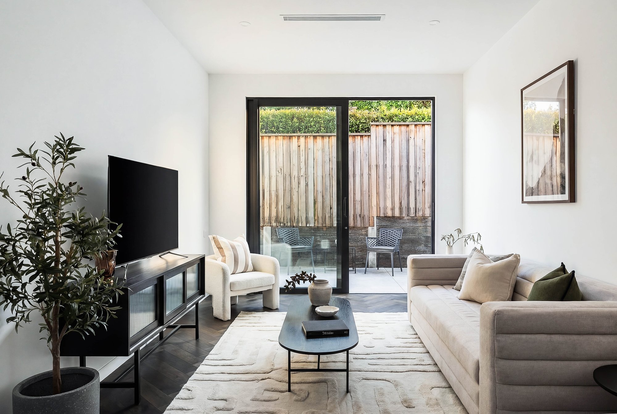 Living area with concrete floors, American oak joinery, and black steel-framed doors opening to landscaped courtyard.