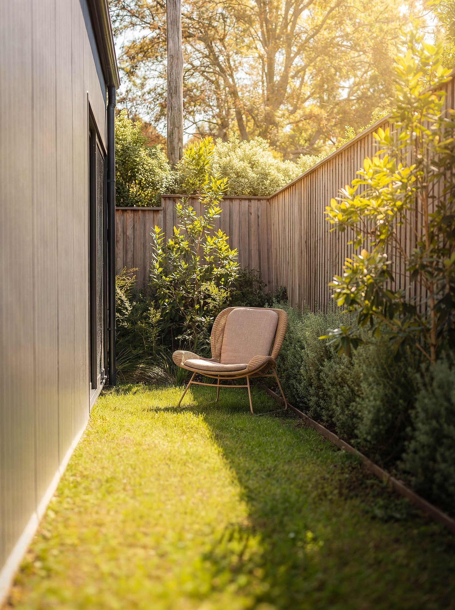 Timber chair on lawn beside vertical timber fence with dappled afternoon light through established trees.