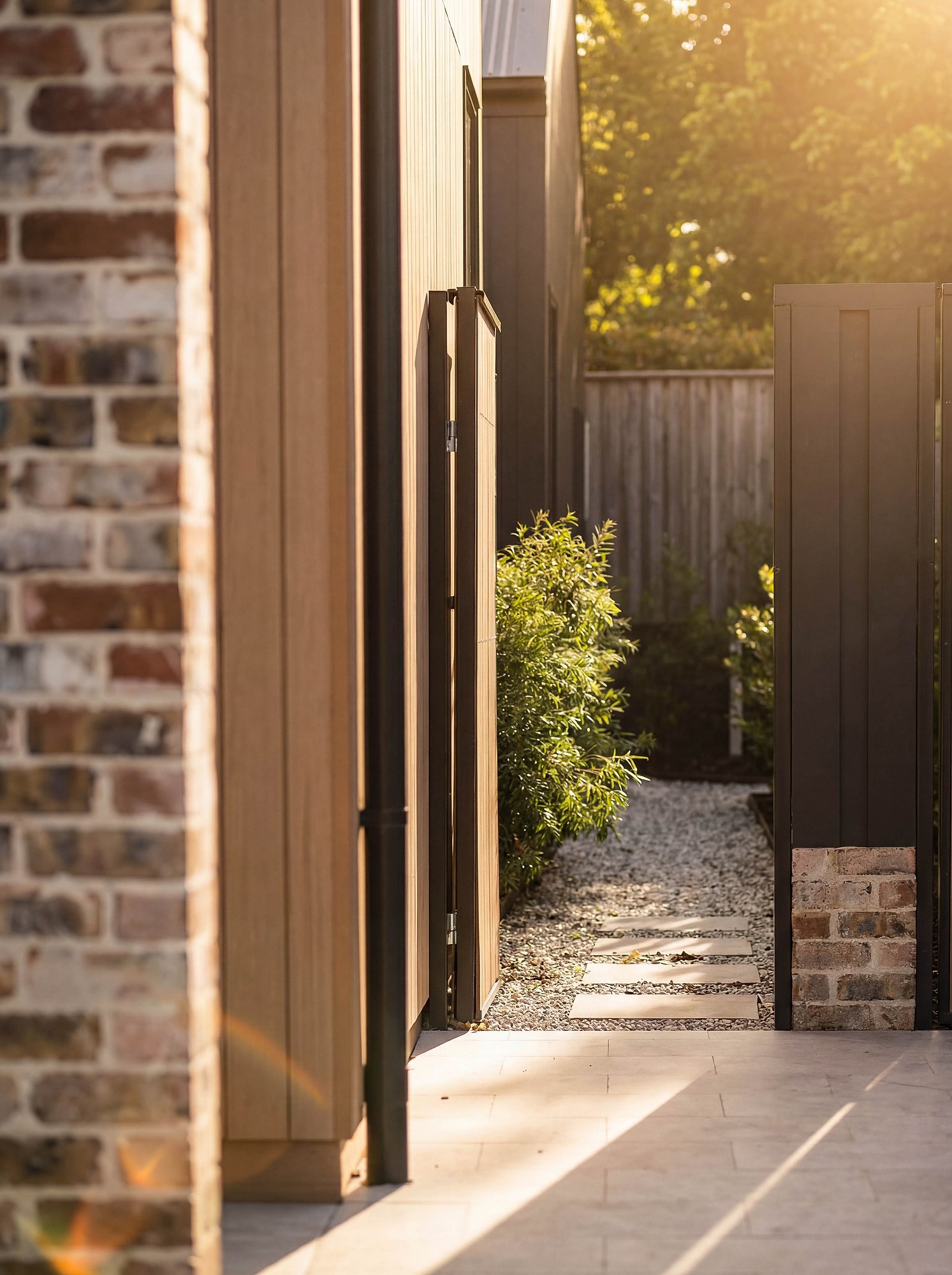 Timber-framed doorway opening to garden path, with recycled brick walls and golden afternoon light filtering through established plantings.