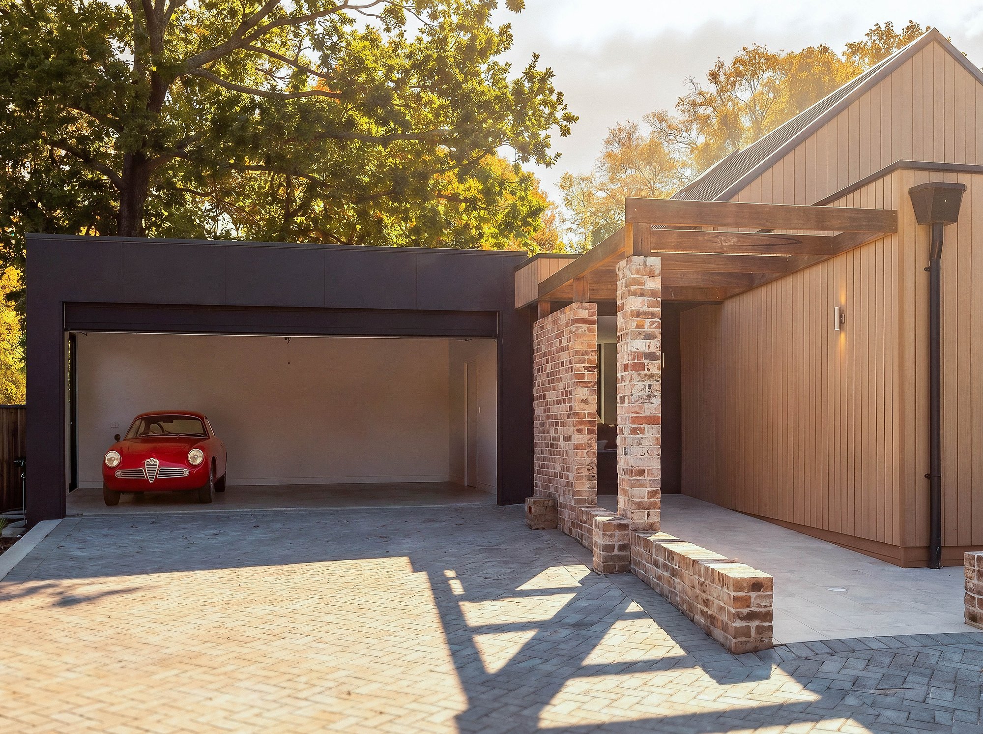 Contemporary garage with recycled brick entry wall and vertical timber cladding, featuring paved driveway and established tree canopy.
