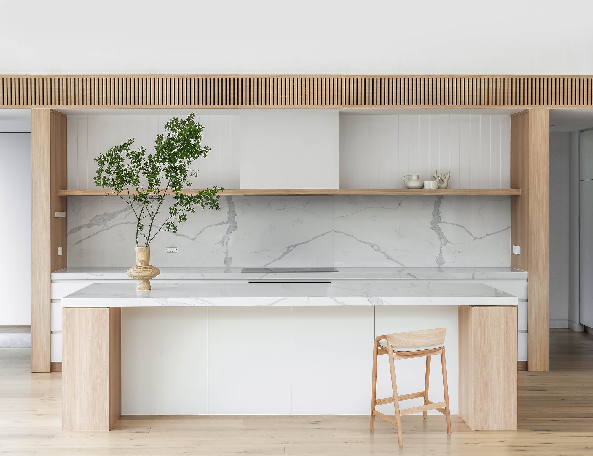 Modern kitchen featuring white marble island, timber cabinetry with fluted wood ceiling detail, and minimalist design with natural materials.