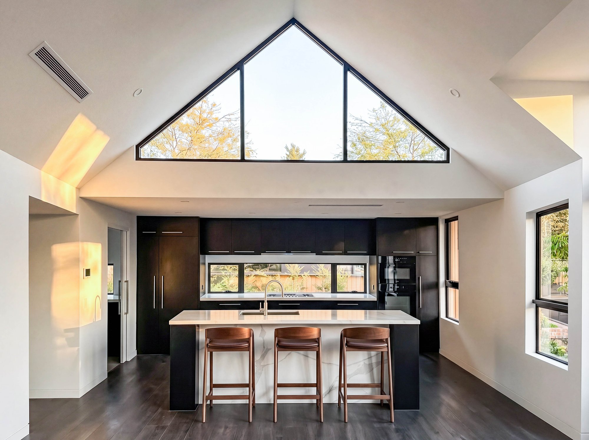 Open-plan kitchen with American oak island, dark timber joinery and triangular clerestory window above.