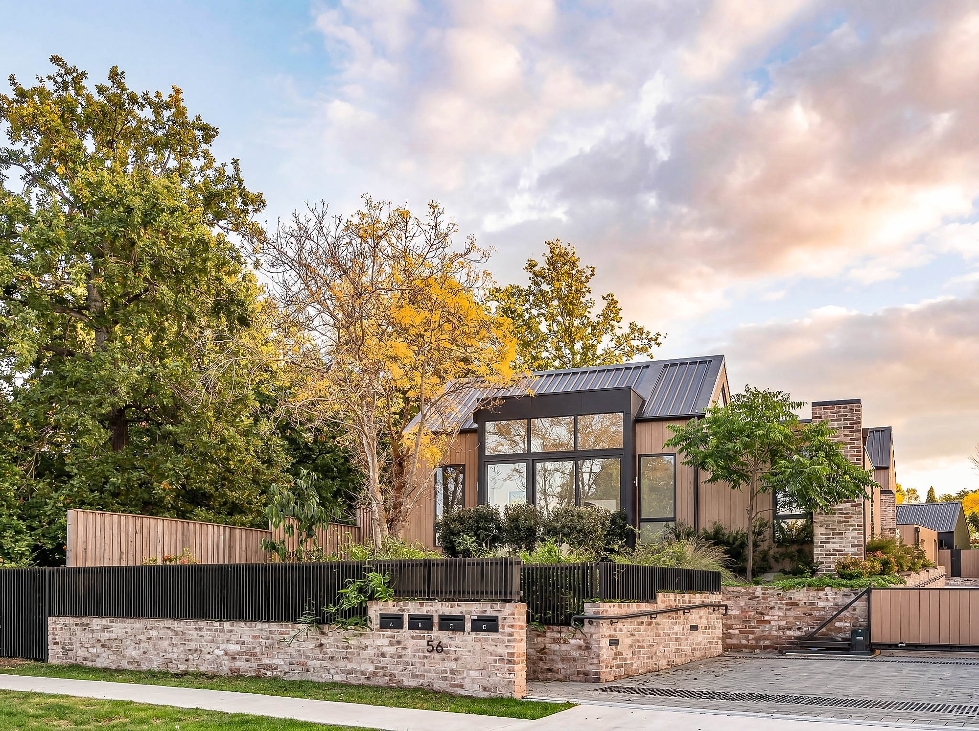 Contemporary home with glazed pavilion extension, sandstone retaining wall, and established native trees under evening sky.