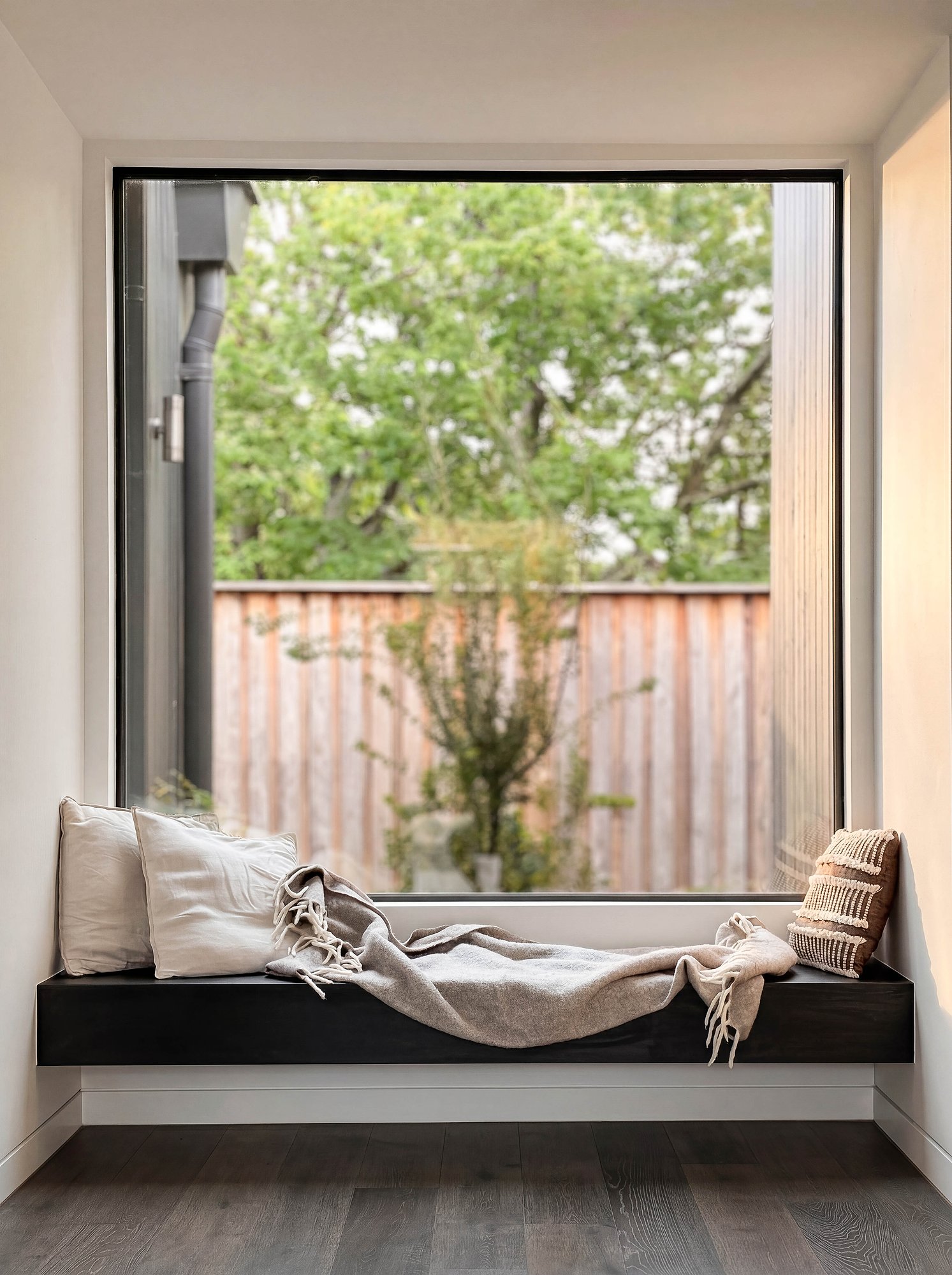 Built-in window seat with dark timber frame overlooking established garden through full-height glazing.
