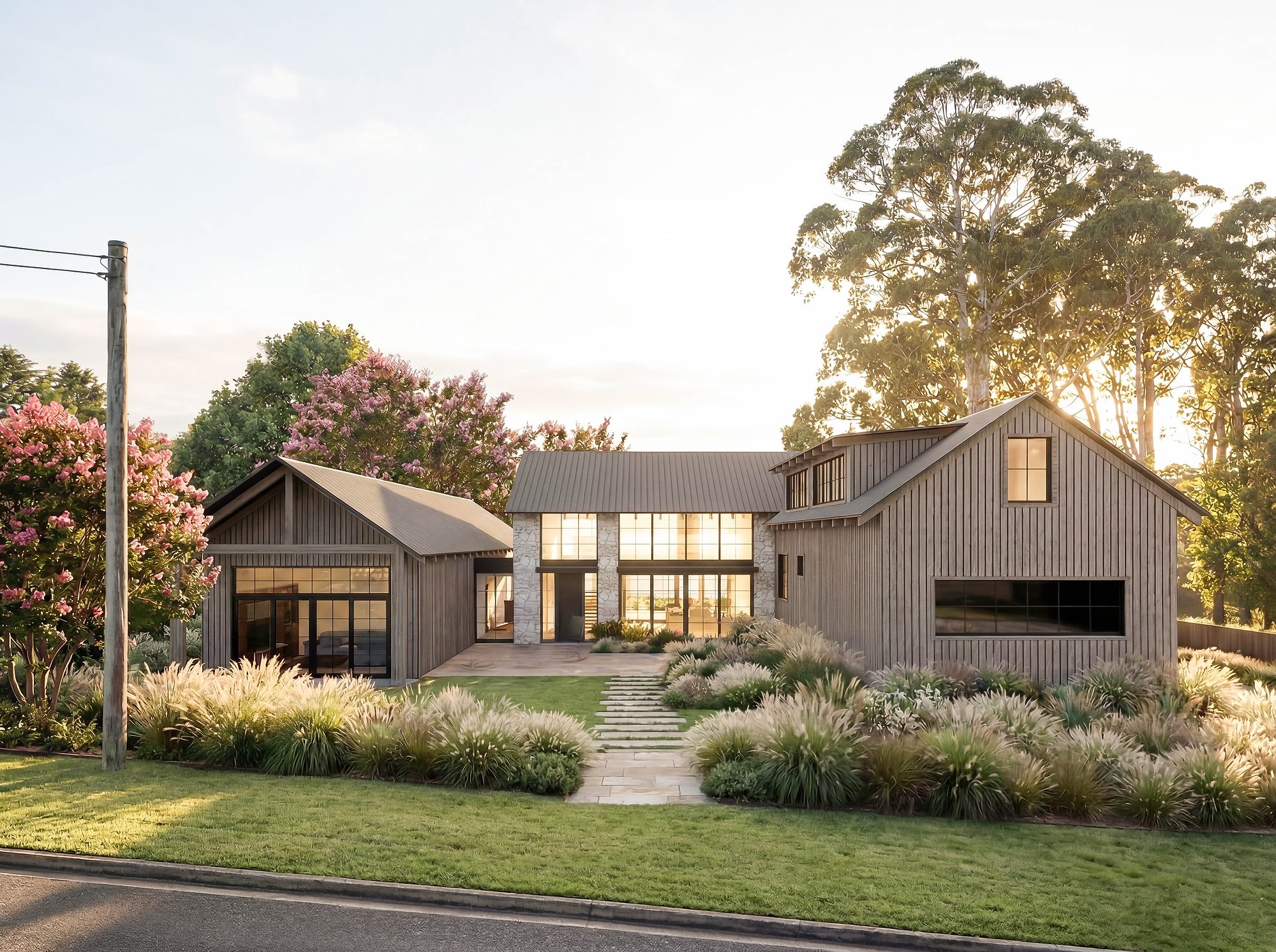 Contemporary home in weatherboard and black steel cladding with established garden plantings and afternoon light filtering through mature eucalyptus.