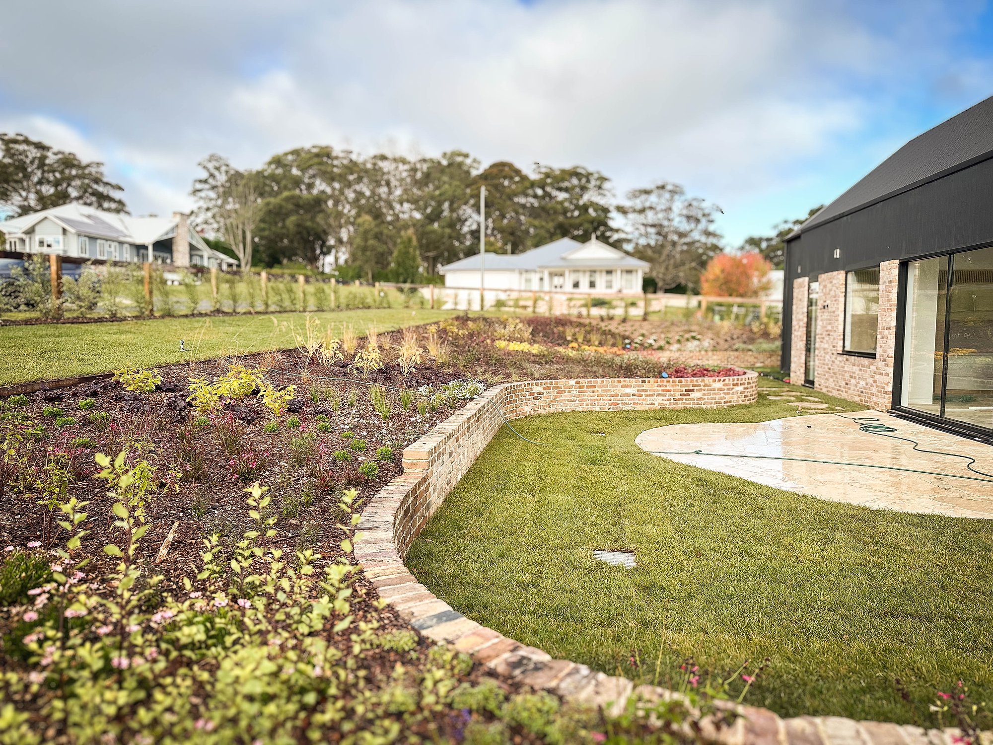 Sandstone retaining walls define planted beds around a contemporary pavilion with established gums beyond.
