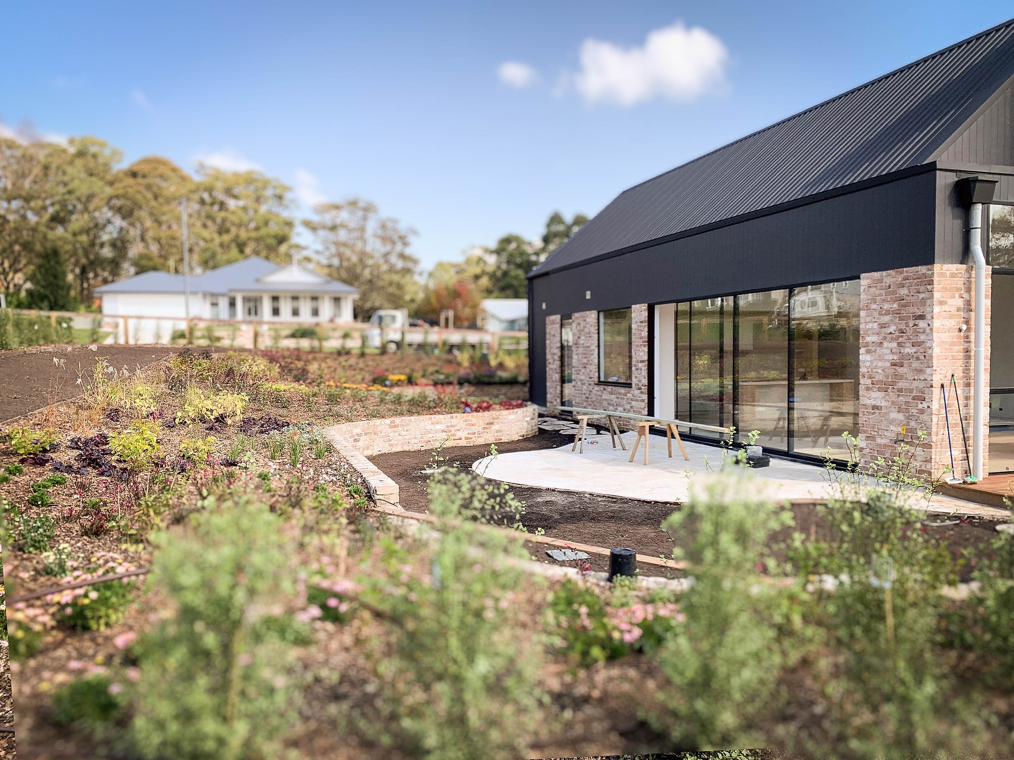 Modern pavilion with recycled brick and dark metal roofing set within native garden plantings and established trees.