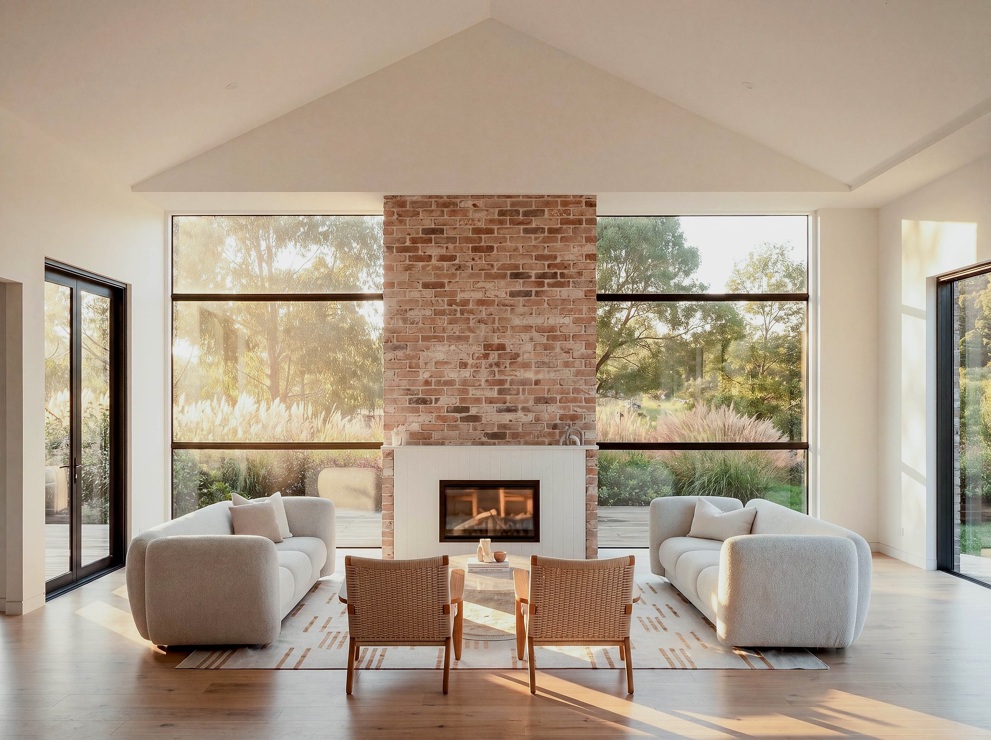 Open-plan living room with recycled brick fireplace, concrete floors, and floor-to-ceiling glazing framing rural views.